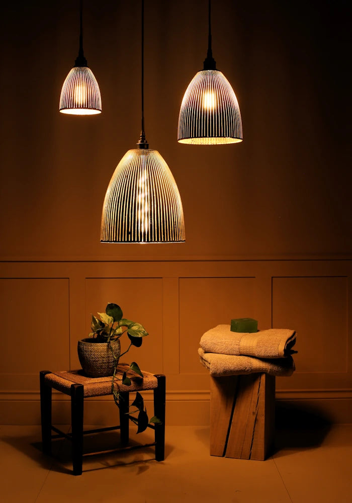 Cluster of 3 large black and gold ribbed glass bathroom pendant lights casting shadows on plant and towels 