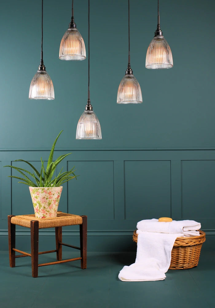 A cluster of five small bell prismatic glass bathroom pendant lights switched off with green plant and towels in a basket.