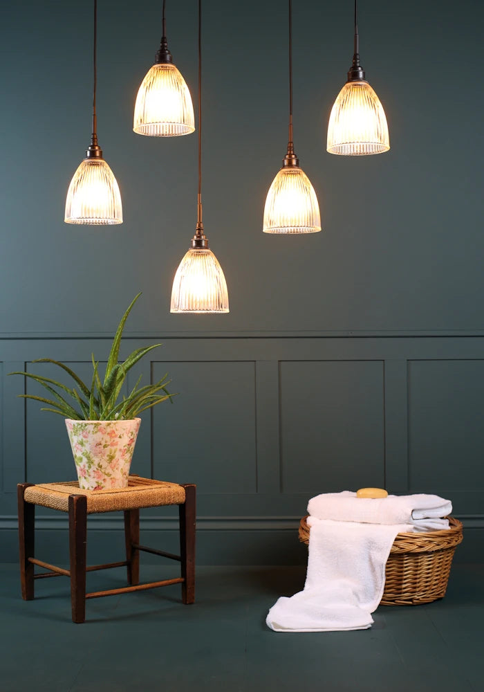 A cluster of five small bell prismatic glass bathroom pendant lights with green plant and towels in a basket.