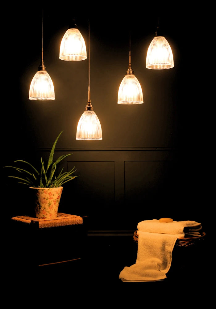 A cluster of five small bell prismatic glass bathroom pendant lights casting shadows on green plant and towels in a basket.