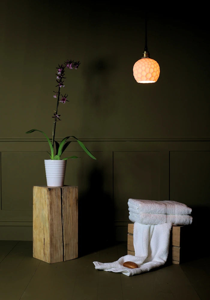 Beehive style porcelain bathroom pendant light casting shadows onto decorative plant and bath towels.