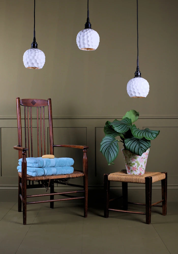 Triple cluster of beehive style porcelain bathroom pendant lights switched off with wooden chair, bath towels and plant.