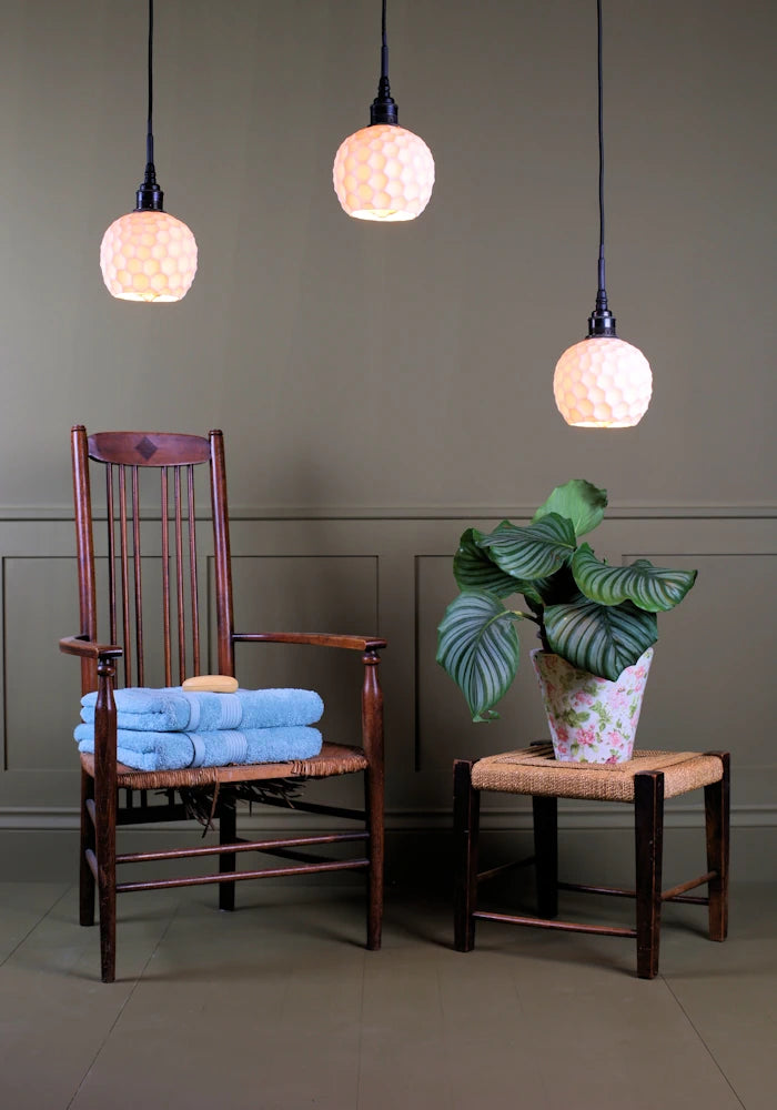 Triple cluster of beehive style porcelain bathroom pendant lights with wooden chair, bath towels and plant.