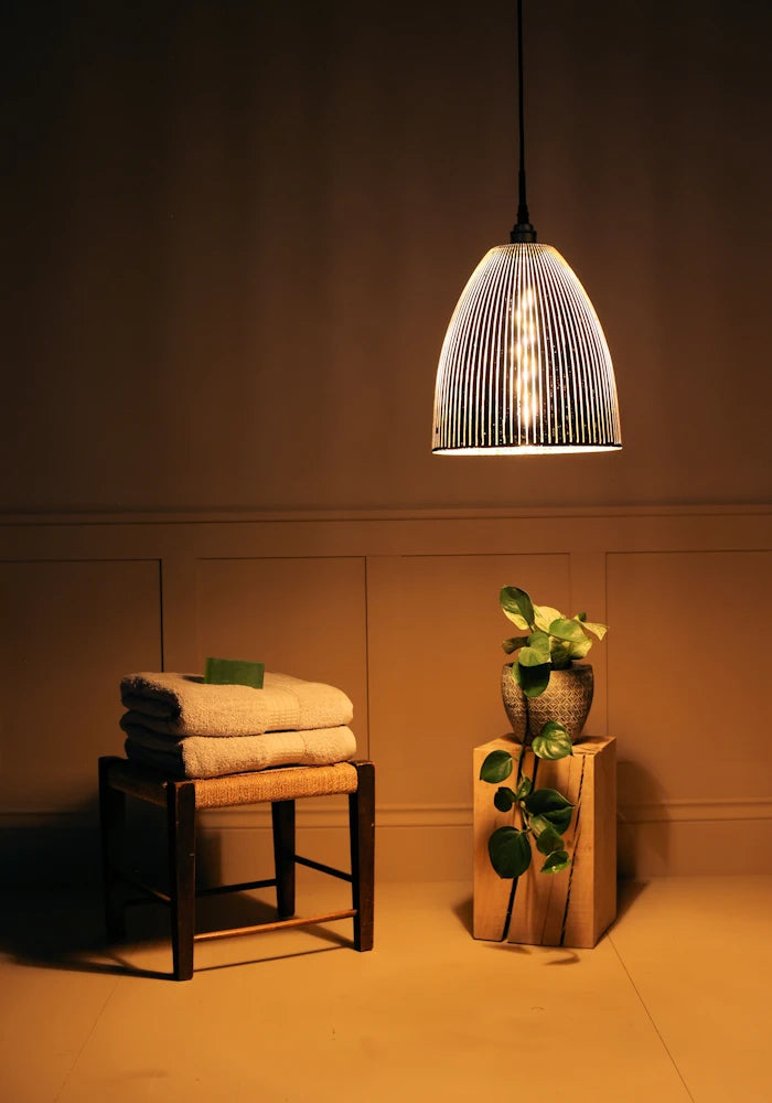 Large bell shaped black and gold ribbed glass pendant light casting shadows on towels and plant