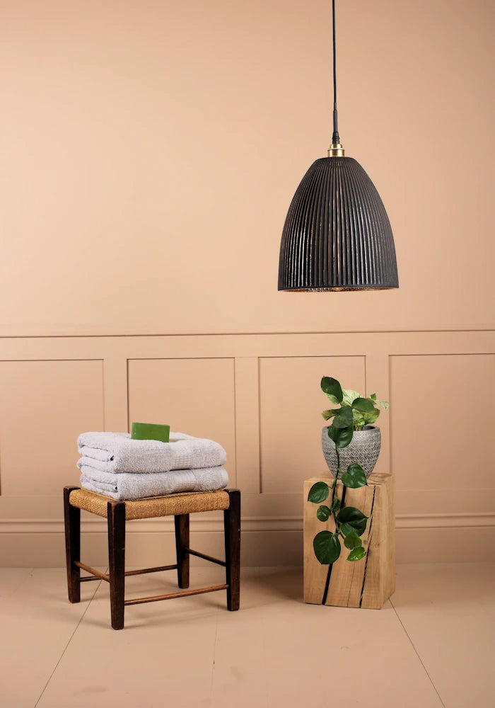 Large bell shaped black and gold ribbed glass pendant light switched off with towels and plant