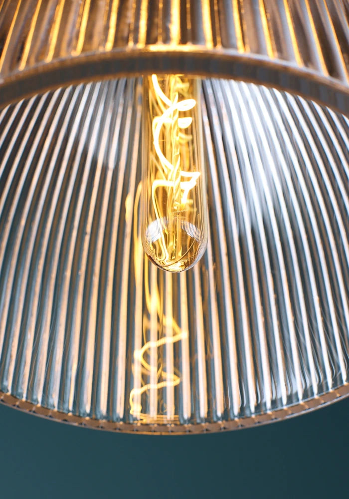 Close up spiral filament light bulb in large bell ribbed glass bathroom pendant light.