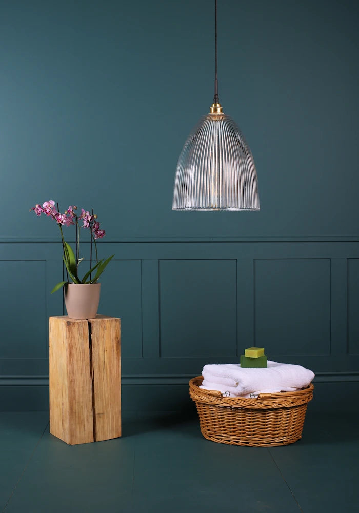 Large bell shaped ribbed glass bathroom pendant light switched off with pink flowers and basket with towels