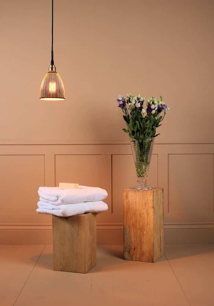 Small black and gold bell shaped ribbed glass bathroom pendant light with towels and vase of flowers 