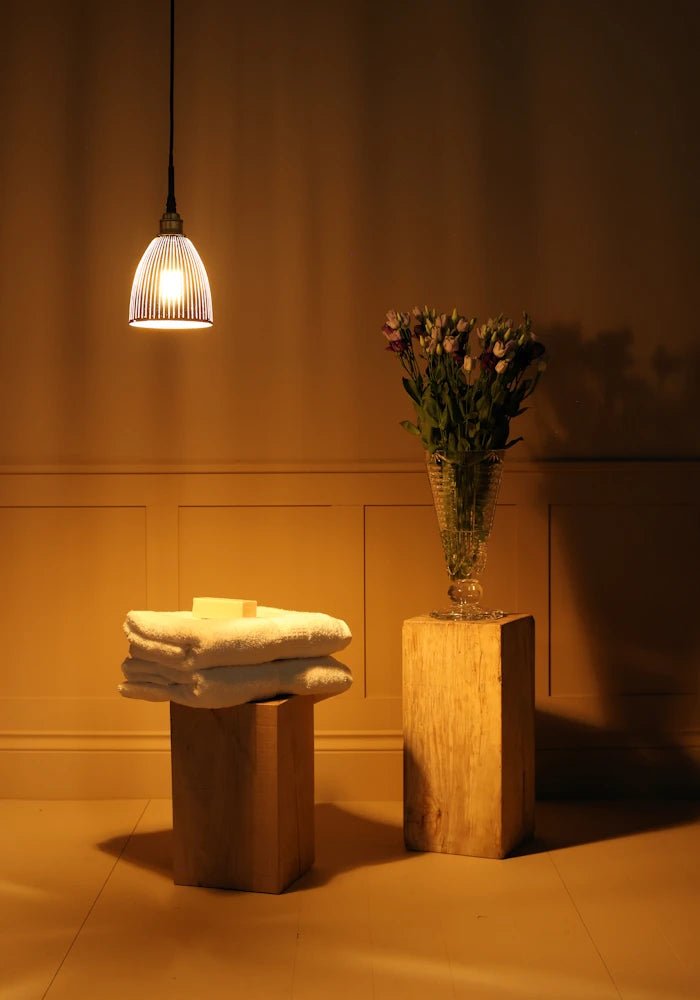 Small black and gold bell shaped ribbed glass bathroom pendant light with towels and vase of flowers 