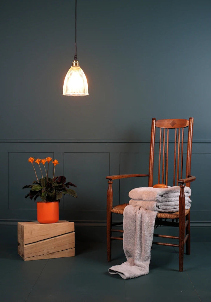 Small bell shaped glass bathroom pendant light with wooden chair and orange flowers 