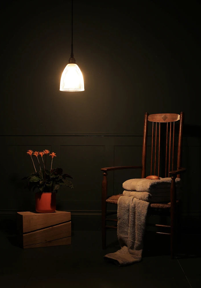 Small bell shaped glass bathroom pendant light casting shadows onto wooden chair and orange flowers