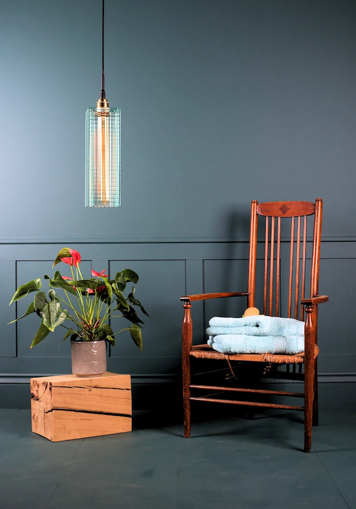 Large ribbed glass bathroom pendant light switched off with decorative plant and wooden chair with bath towels