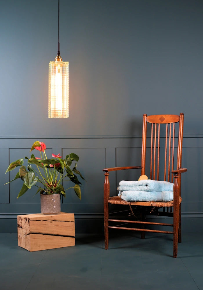 Large ribbed glass bathroom pendant light with decorative plant and wooden chair with bath towels