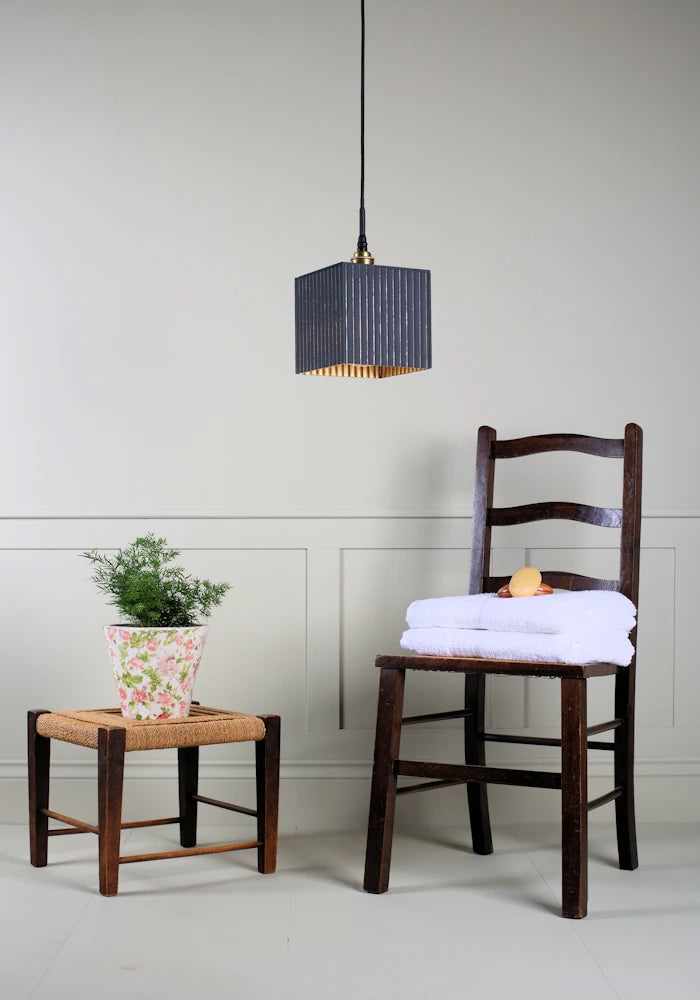 Ribbed glass black and gold leaf bathroom pendant light switched off with plant, wooden chair and bath towels.