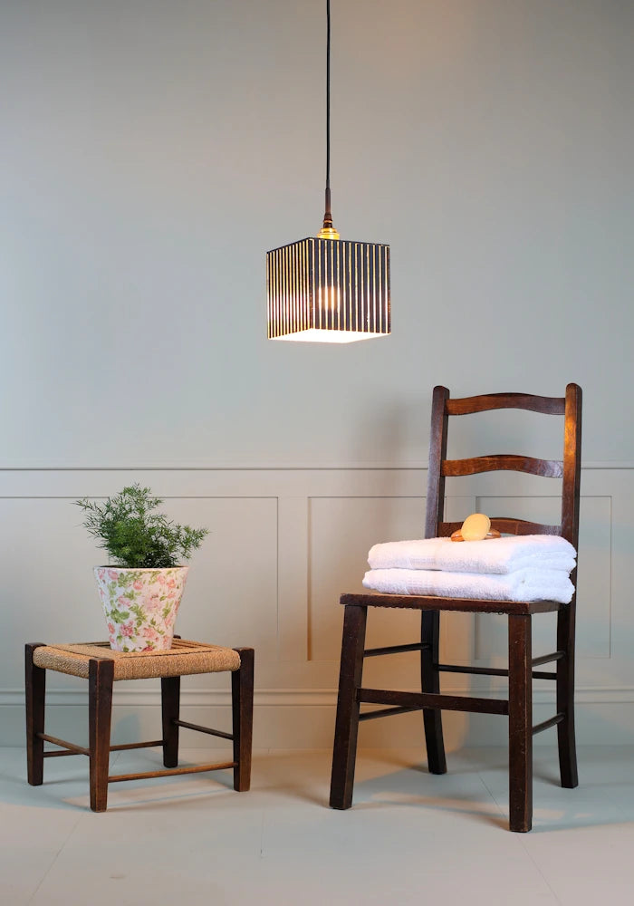 Ribbed glass black and gold leaf bathroom pendant light with plant, wooden chair and bath towels.