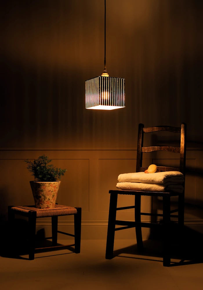 Ribbed glass black and gold leaf bathroom pendant light with plant, wooden chair and bath towels.