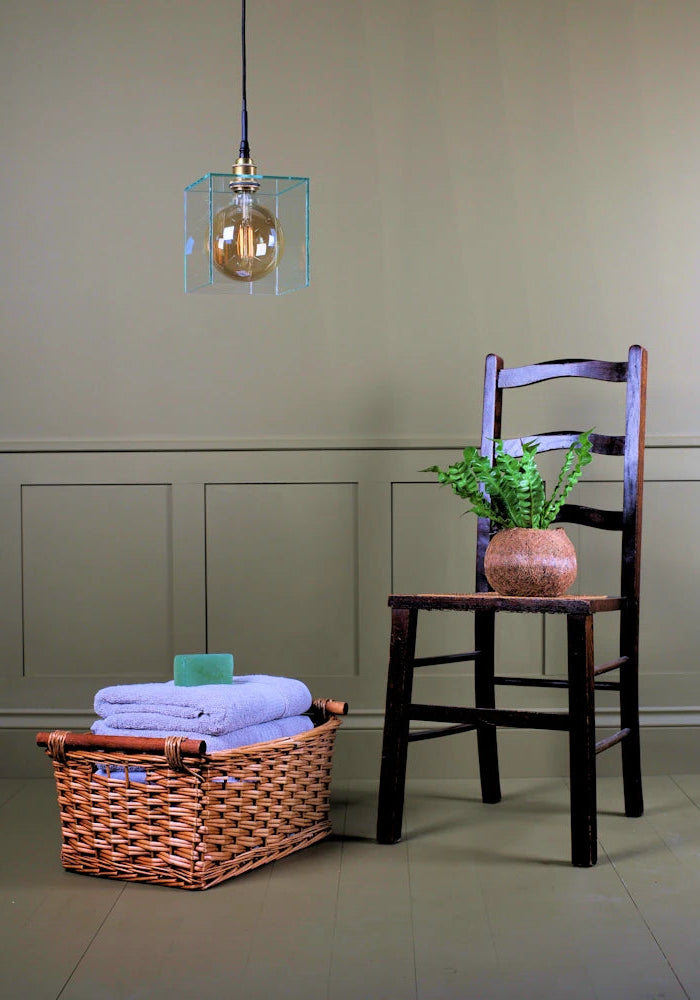 Square clear glass bathroom pendant light switched off with wooden chair, plant and towels 