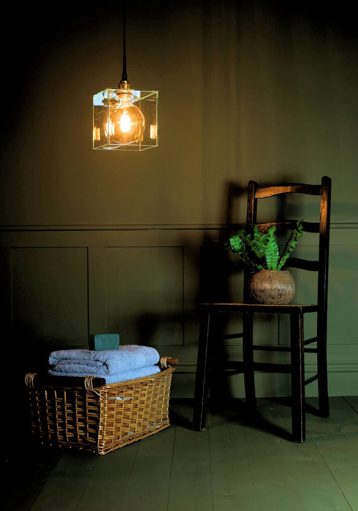 Square clear glass bathroom pendant light with wooden chair, plant and towels 