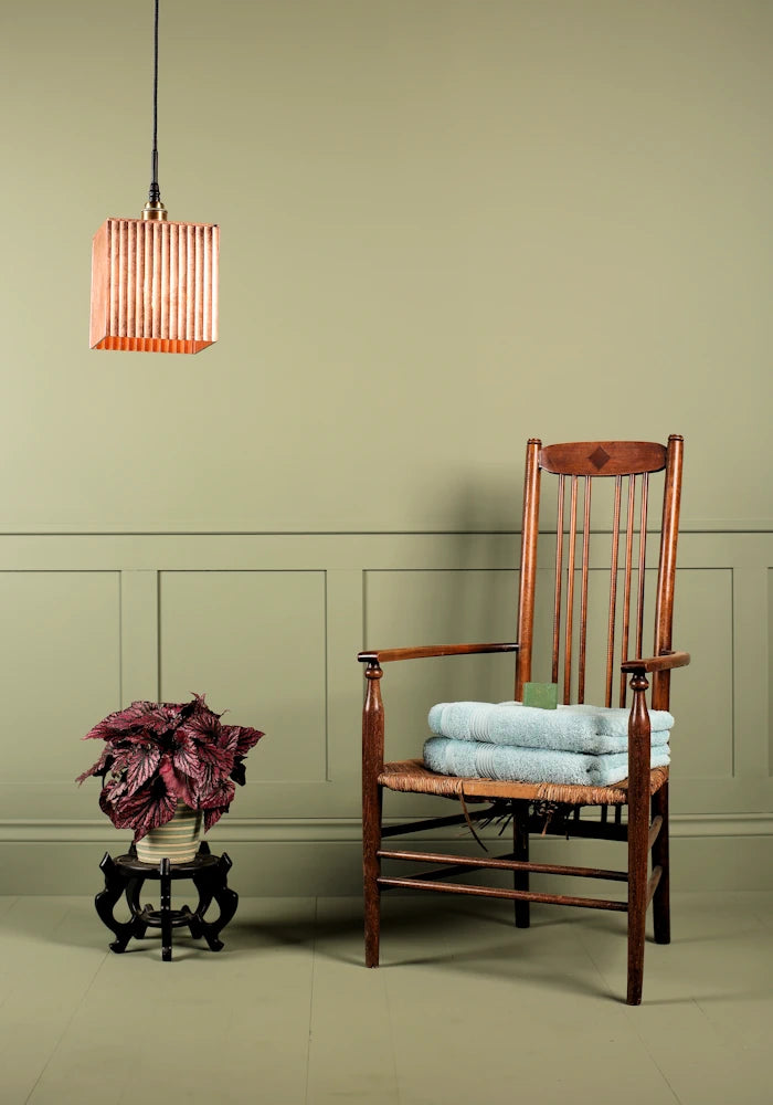 Large cube copper leaf bathroom pendant light switched off, plant, wooden chair and bath towels.