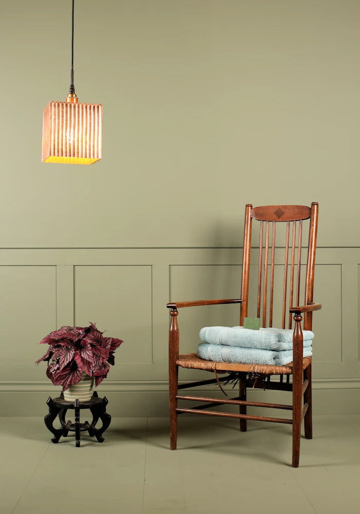 Large cube copper leaf bathroom pendant light, plant, wooden chair and bath towels.