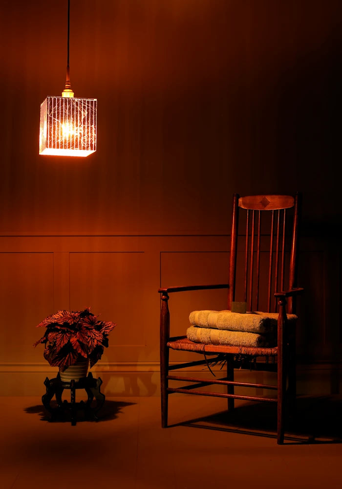 Large cube copper leaf bathroom pendant light casting shadows, plant, wooden chair and bath towels.