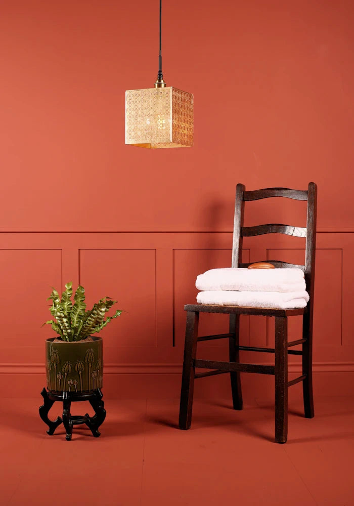 Large square Moroccan patterned gold bathroom pendant light switched off, plant and wooden chair with towels.