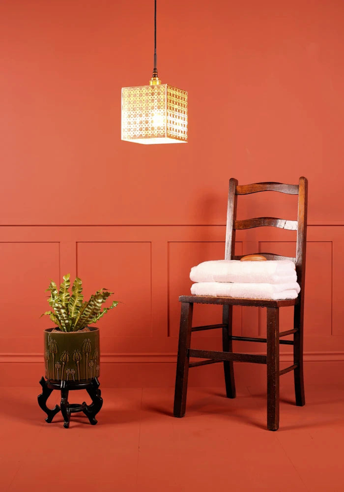 Large square Moroccan patterned gold bathroom pendant light, plant and wooden chair with towels.