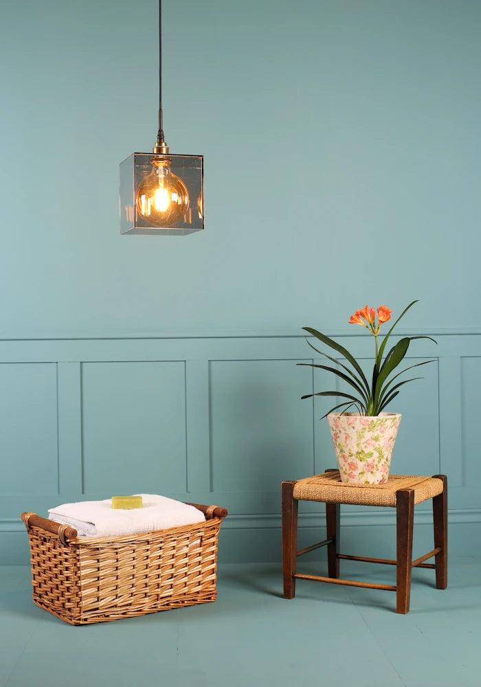 Large square smoked glass bathroom pendant light, basket of bath towels and plant.