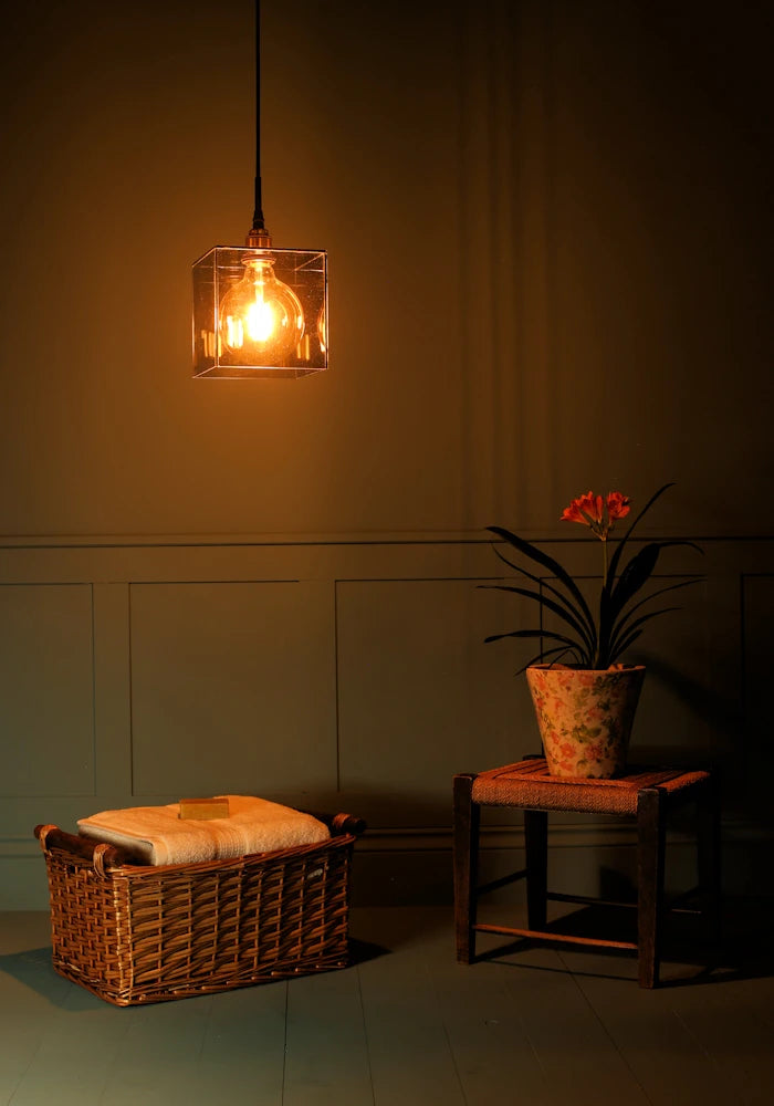 Large square smoked glass bathroom pendant light casting shadows, basket of bath towels and plant.