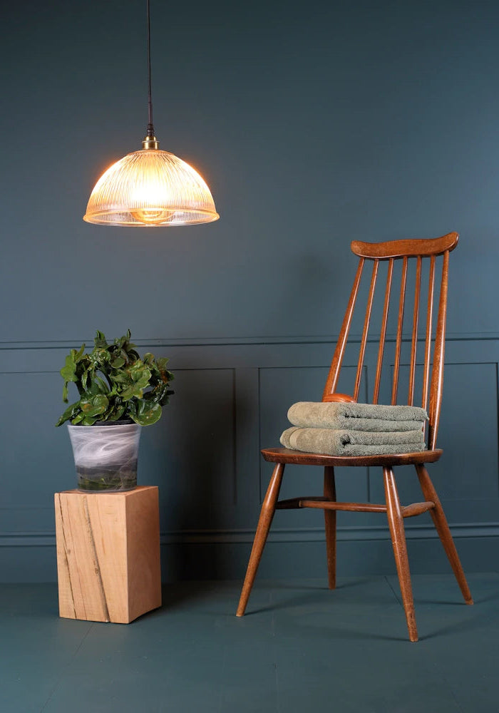 A large decorative ribbed glass dome bathroom pendant light with chair and plant