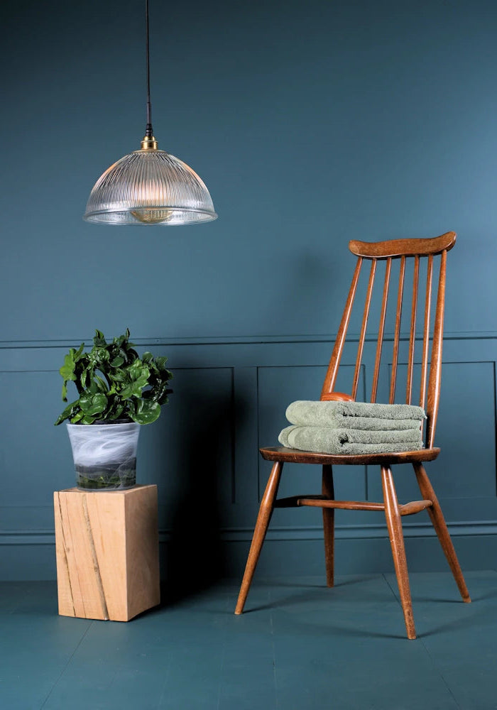 A large decorative ribbed glass dome bathroom pendant light switched off with chair and plant