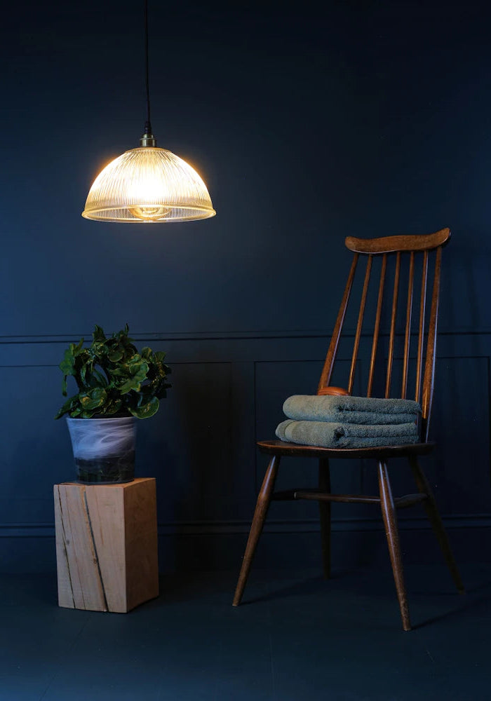 A large decorative ribbed glass dome bathroom pendant light casting shadows onto chair and plant