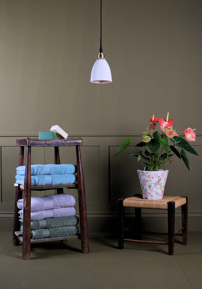 Conical ribbed porcelain bathroom pendant light switched off with bath towels and plant.