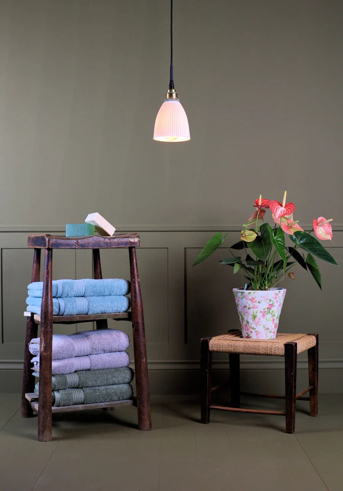 Conical ribbed porcelain bathroom pendant light with bath towels and plant.