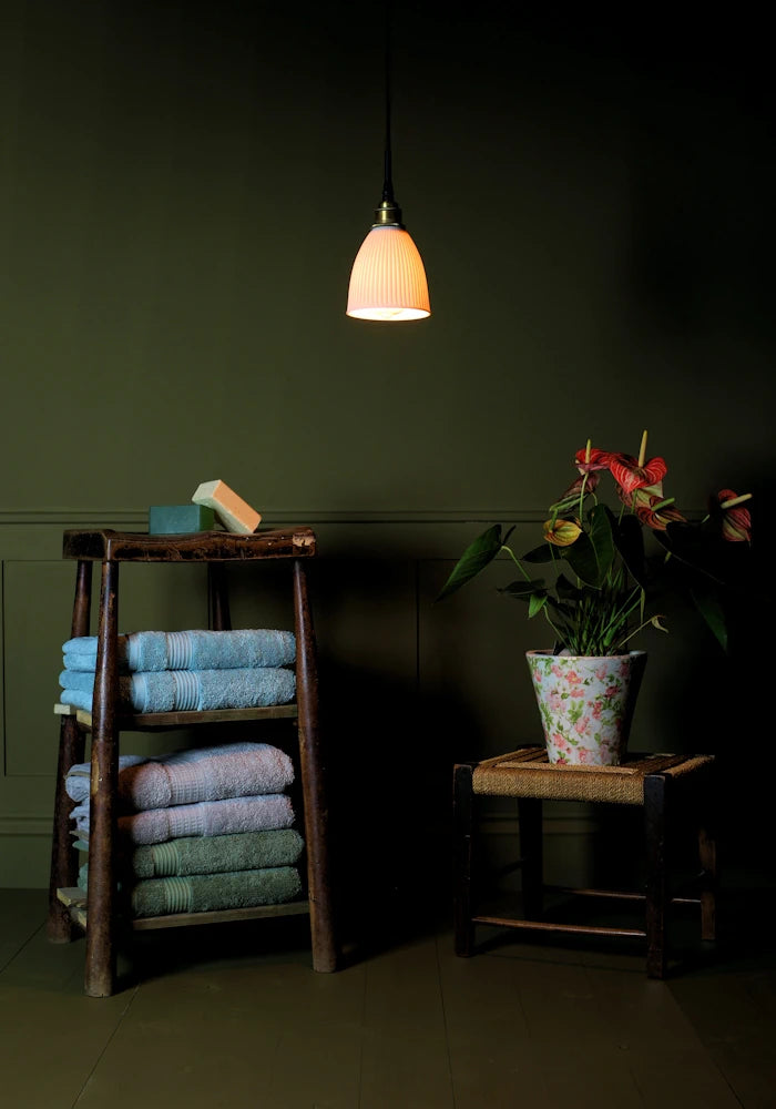 Conical ribbed porcelain bathroom pendant light casting shadows onto bath towels and plant.