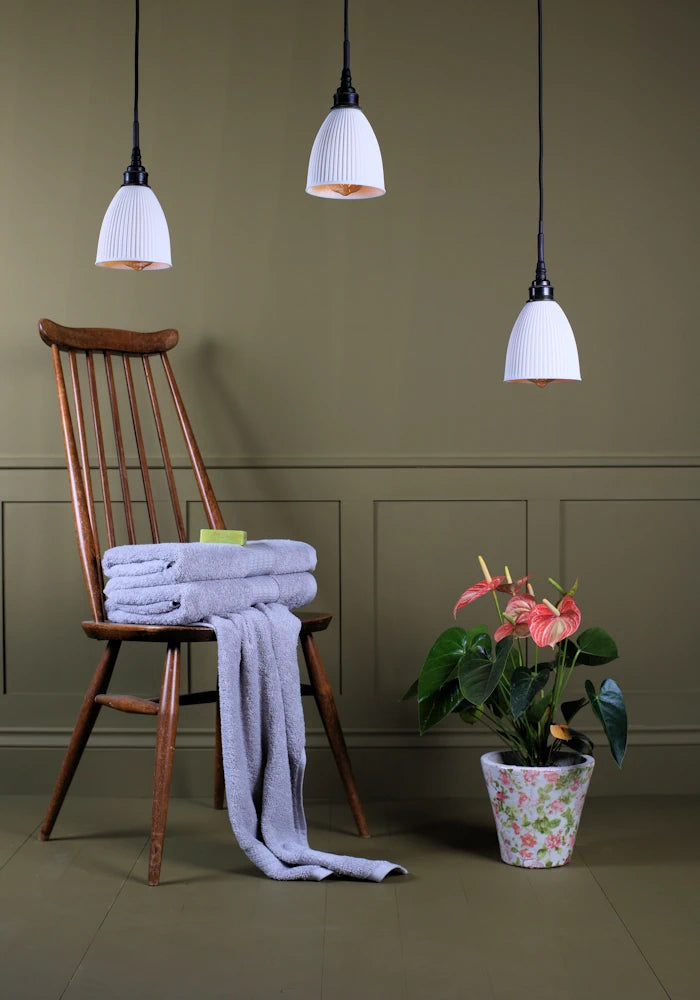 Triple porcelain cluster bathroom pendant light switched off with wooden chair, bath towels and plant.