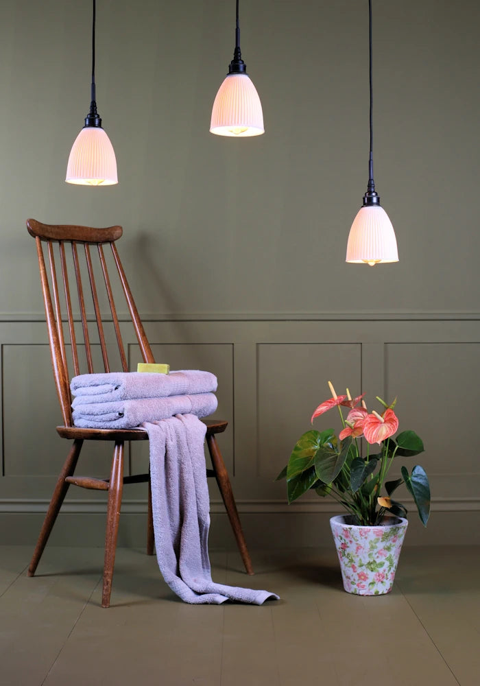 Triple porcelain cluster bathroom pendant light with wooden chair, bath towels and plant.