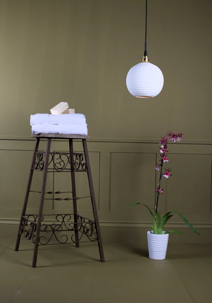 Large spherical porcelain bathroom pendant light switched off with bath towels and exotic plant.