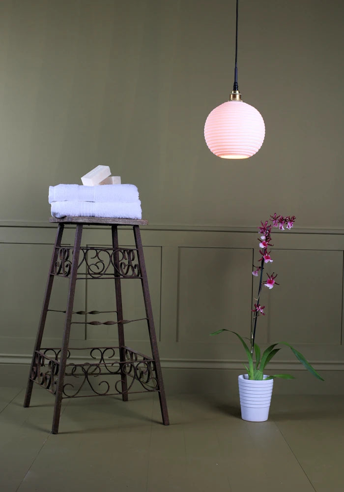 Large spherical porcelain bathroom pendant light with bath towels and exotic plant.