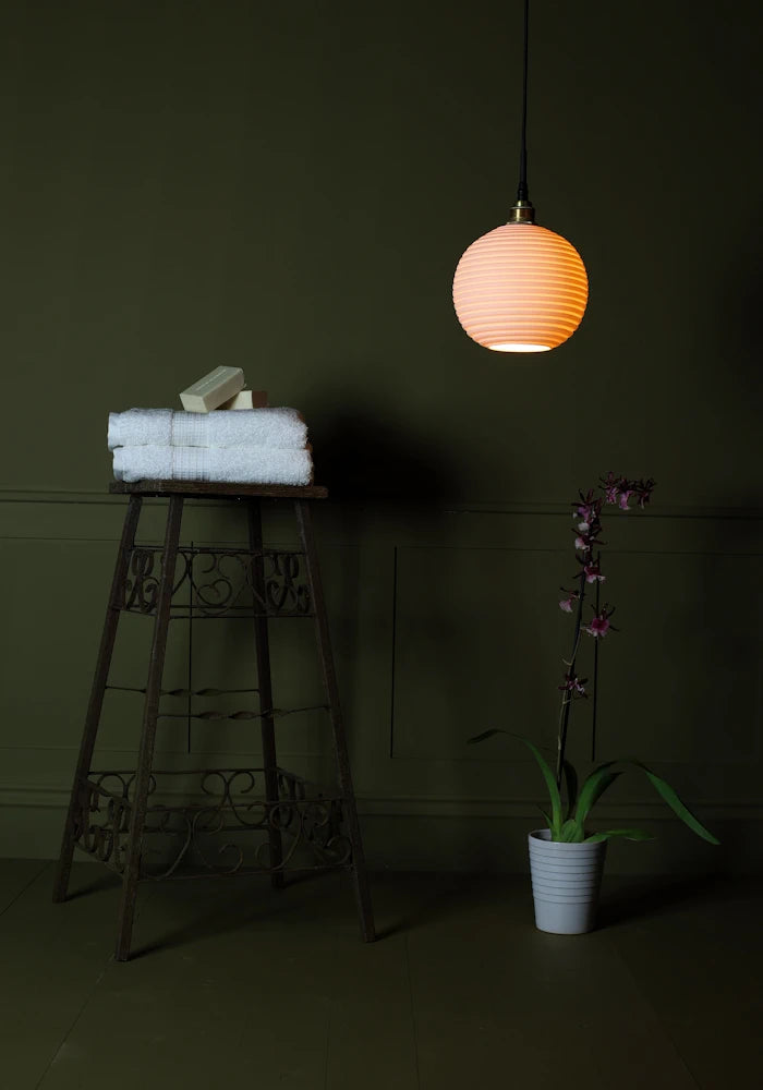 Large spherical porcelain bathroom pendant light casting shadows onto bath towels and exotic plant.