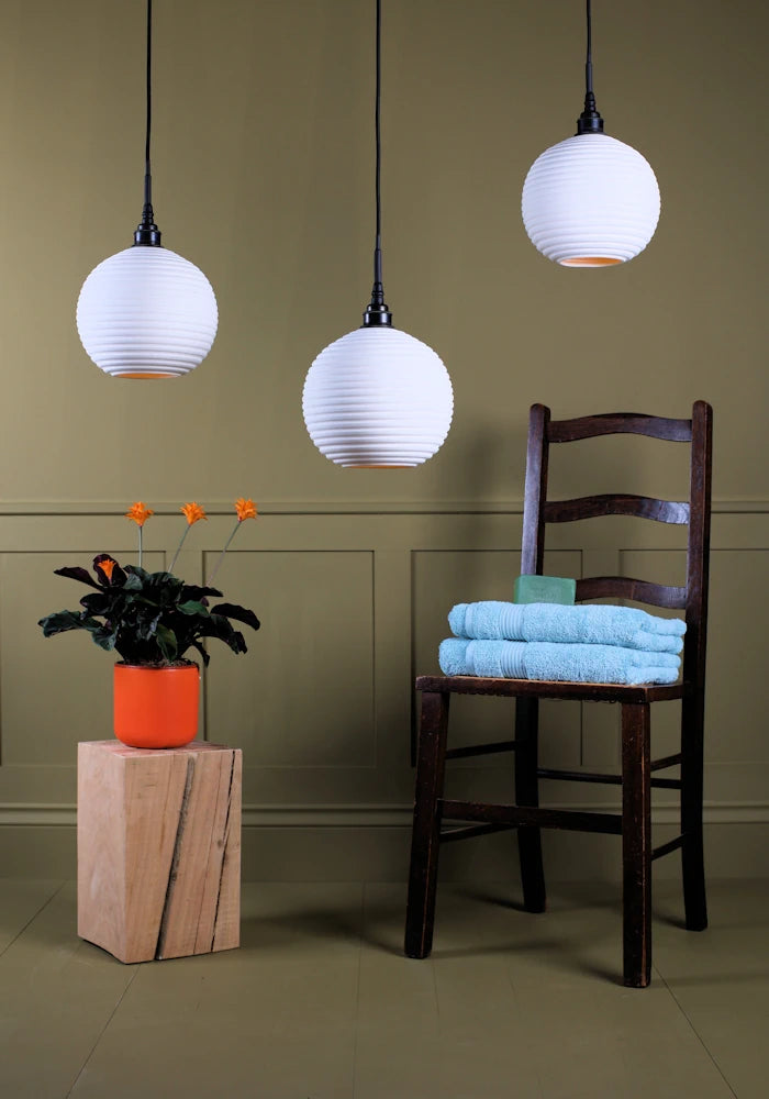 Large triple spherical porcelain bathroom pendant light cluster switched off with plant, wooden chair and bath towels.