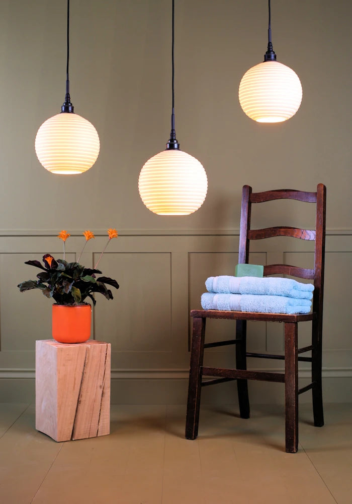 Large triple spherical porcelain bathroom pendant light cluster with plant, wooden chair and bath towels.