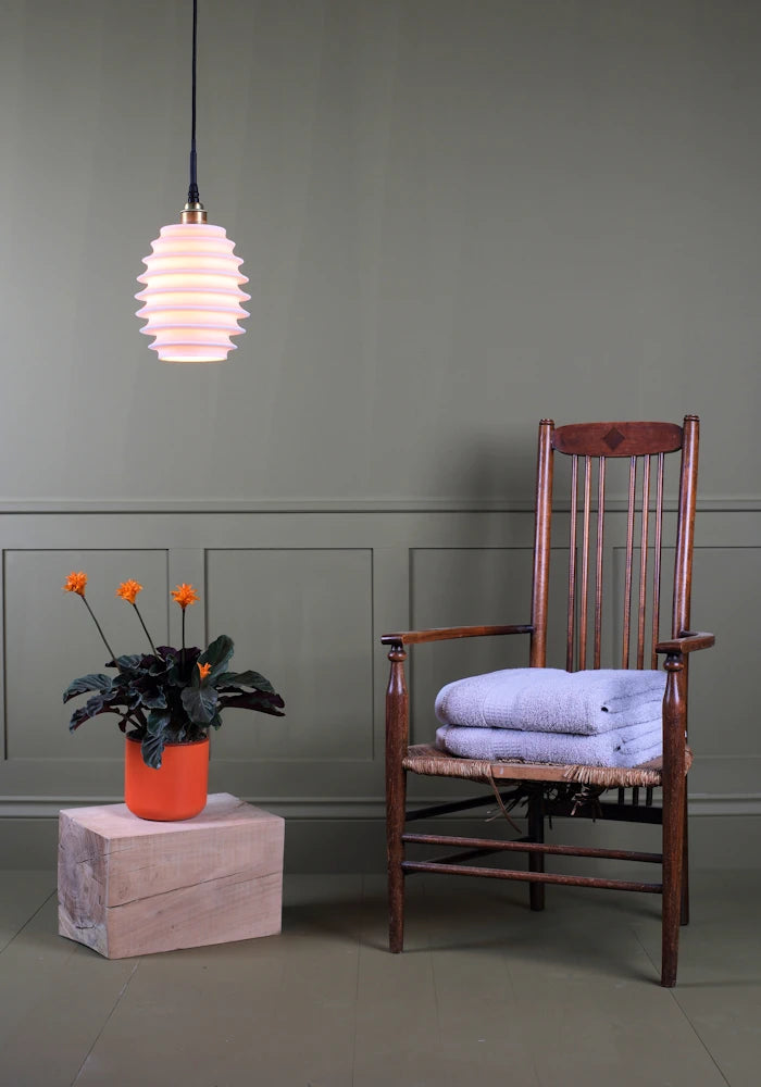 Concertina style porcelain bathroom pendant light with plant, wooden chair and bath towels.