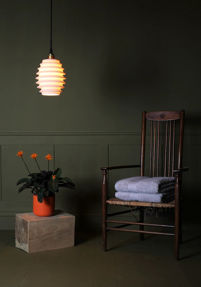 Concertina style porcelain bathroom pendant light with plant, wooden chair and bath towels.