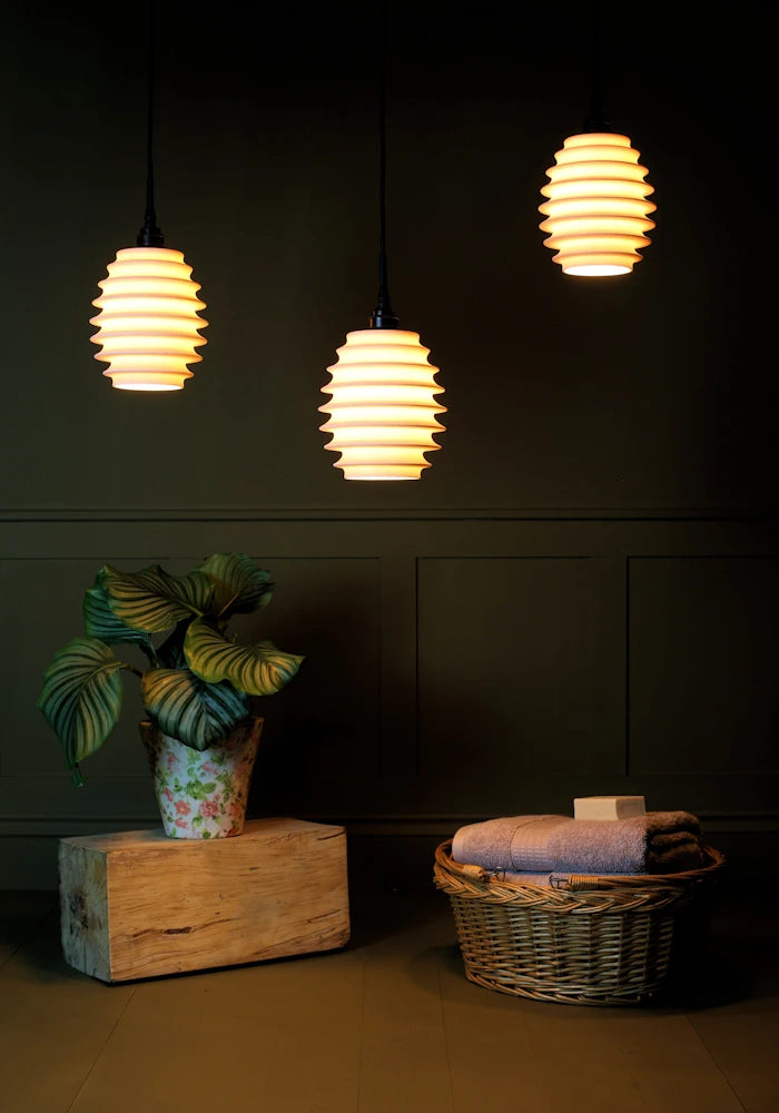 Concertina style porcelain cluster bathroom pendant light casting shadows onto plant and basket of bath towels