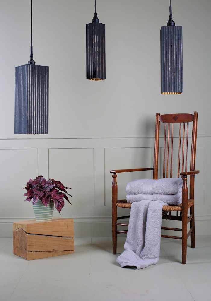 Triple black and gold bathroom pendant light cluster switched off with plant, wooden chair and bath towels. 