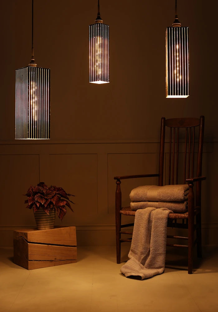 Triple black and gold bathroom pendant light cluster with plant, wooden chair and bath towels. 