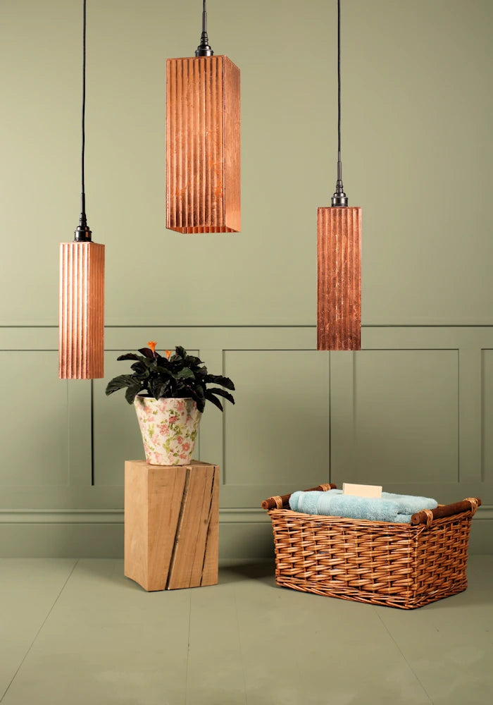 Large triple rectangular copper leaf cluster bathroom pendant light switched off, plant and basket of bath towels. 