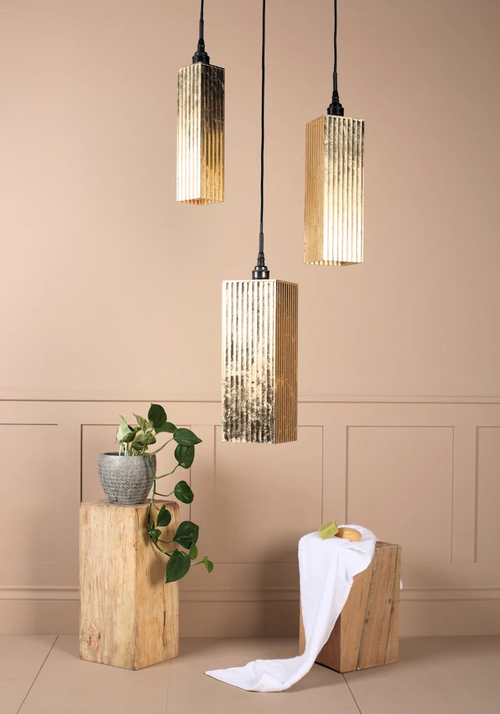 Triple gold leaf bathroom pendant light cluster casting shadows onto plant and bath towel.