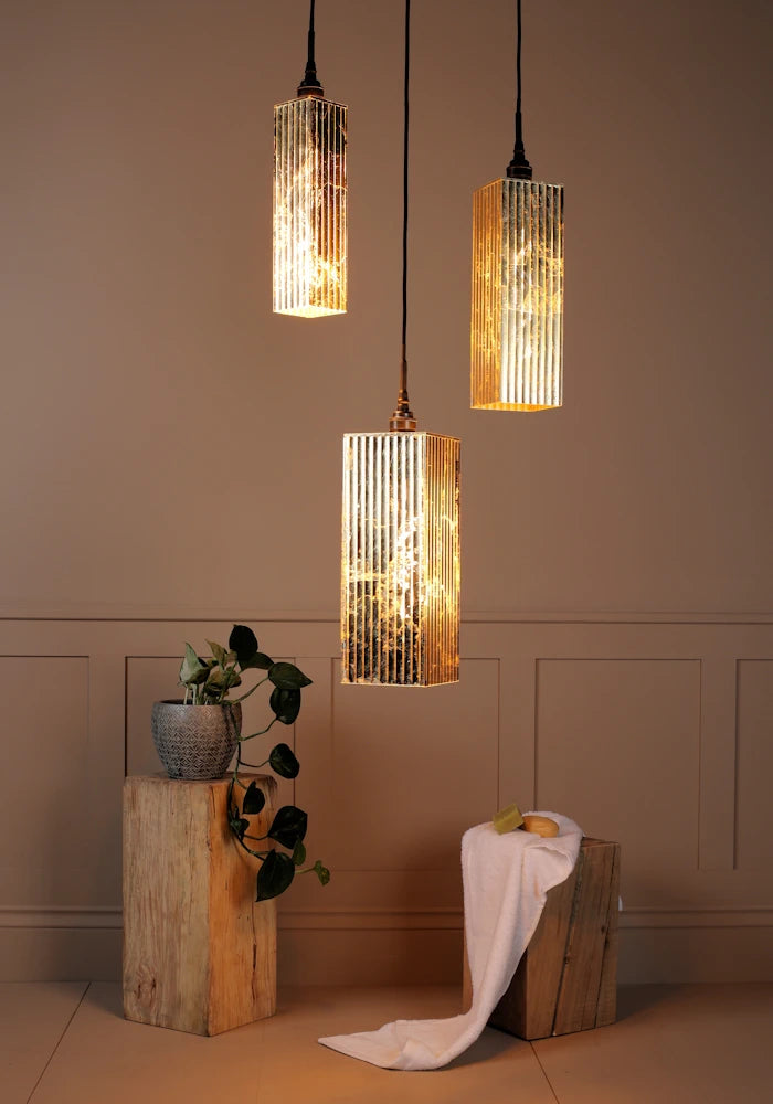 Triple gold leaf bathroom pendant light cluster casting shadows onto plant and bath towel.